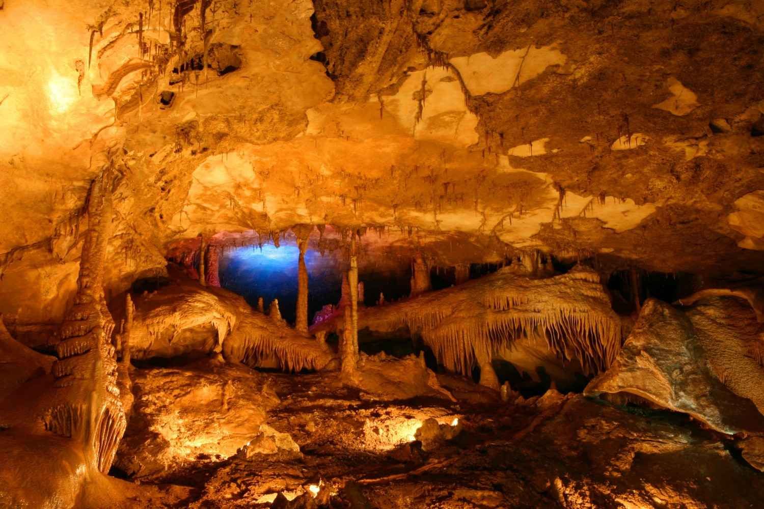 Interior de la cueva con iluminación cálida, formaciones rocosas y una abertura azul en el centro.