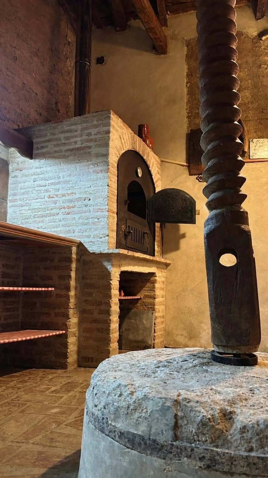 Escena rústica de interior con un horno de ladrillo y una alta chimenea de metal negro en una habitación de tonos cálidos.