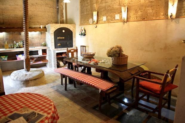 Comedor rústico interior con mesas de madera, bancos, apliques de pared cálidos y un horno de piedra.