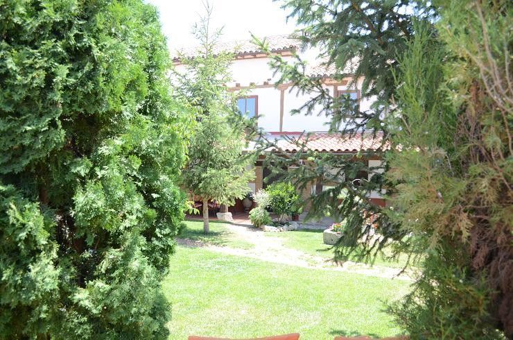 Jardín exuberante con césped verde, árboles y una casa parcialmente visible al fondo.