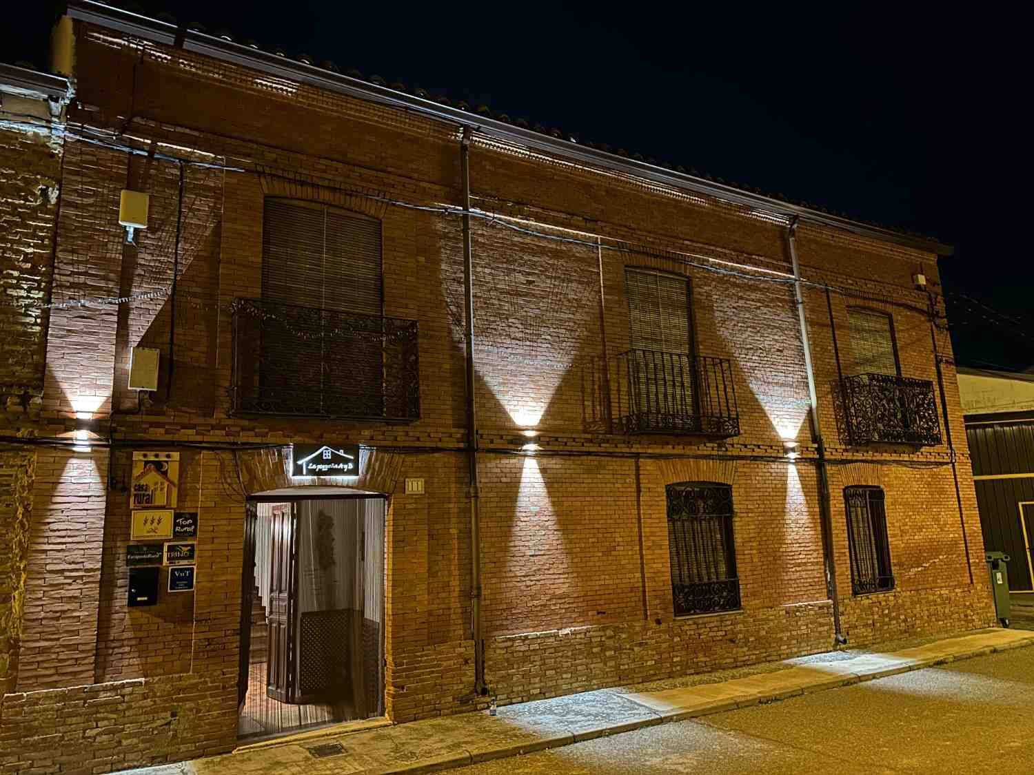 Edificio de ladrillo iluminado por luces exteriores por la noche, con ventanas enrejadas y una entrada central.