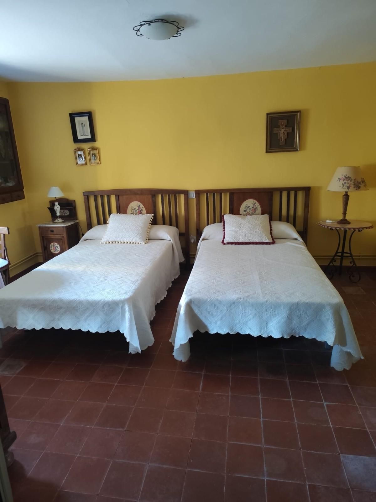 Habitación ordenada con dos camas individuales, paredes amarillas, suelo de baldosas y lámparas de noche.