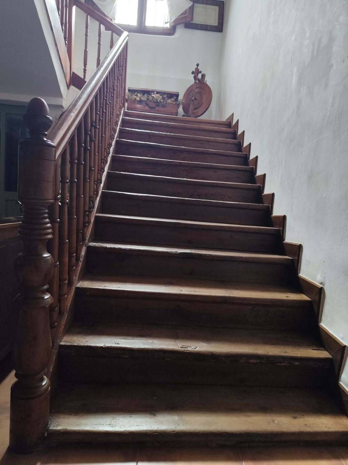 Escalera de madera con barandilla, tenuemente iluminada, en el interior de una vivienda, que conduce a un rellano.