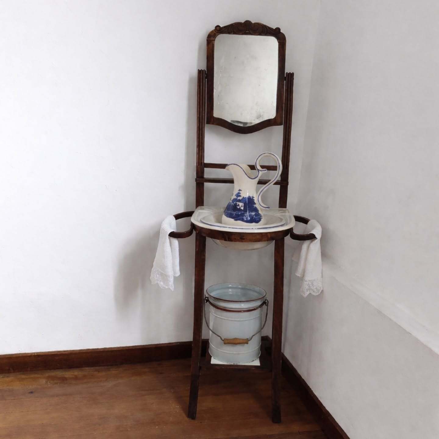 Pequeño lavabo antiguo con espejo, pila y toalla en una esquina contra una pared blanca.