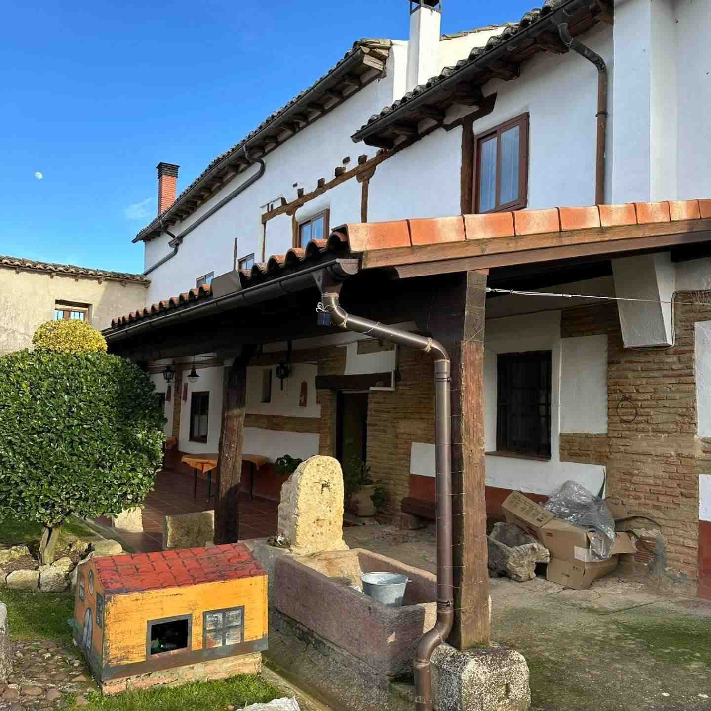 Casa de estuco blanco con porche de baldosas, vigas de madera y una pequeña caseta para perros de color amarillo anaranjado en el patio.