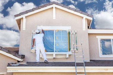 Zwei Männer hängen angeseilt an einem Haus und streichen die Fassade