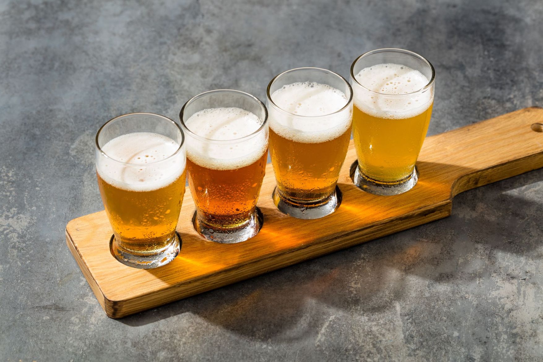 Quatre petits verres de bière blonde mousseuse sur une planche de service en bois