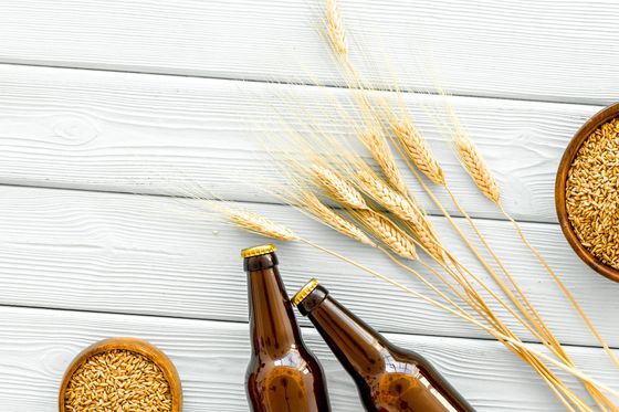 Bouteilles de bière et épis de blé sur une surface en bois clair, avec des bols de grains de céréales