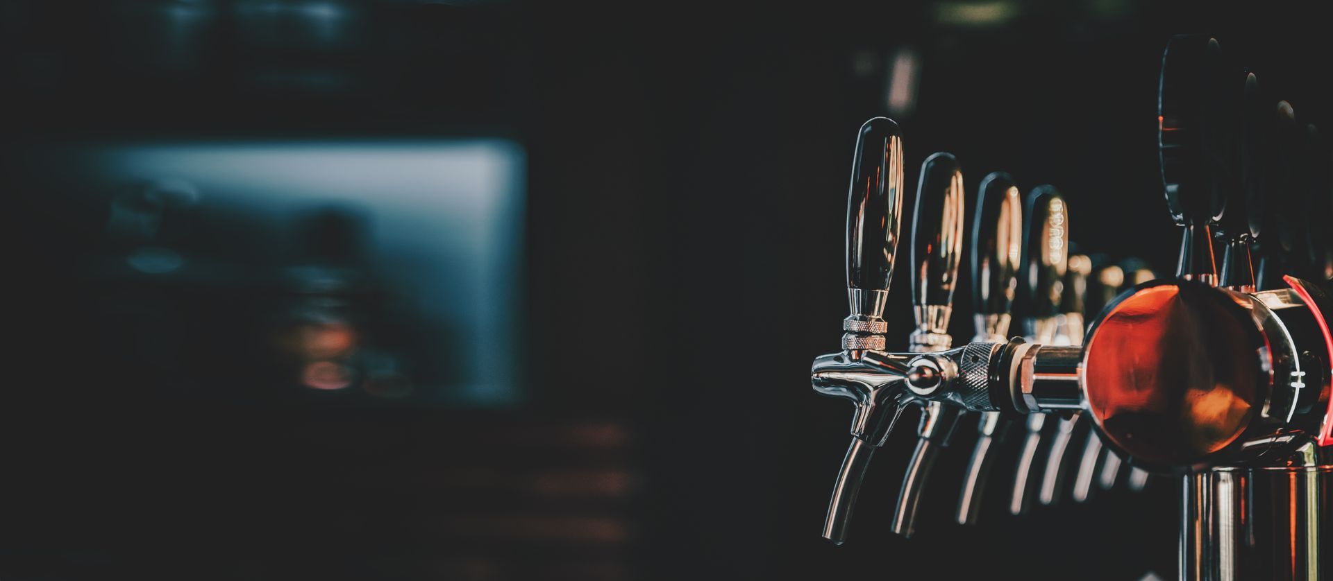Une rangée de tireuses à bière avec une poignée rouge dans un bar faiblement éclairé