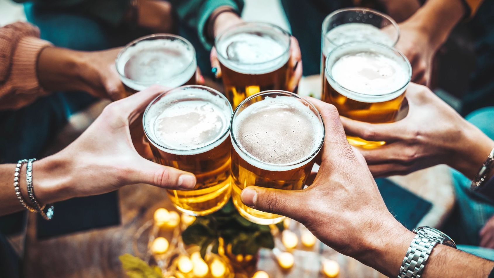 Des amis trinquent à la bière, les mains réunies au-dessus d’une table.
