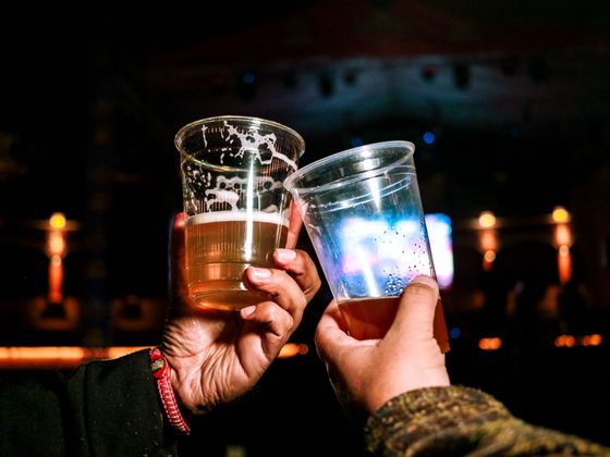 Deux mains trinquant avec des gobelets en plastique remplis de bière lors d’une soirée faiblement éclairée