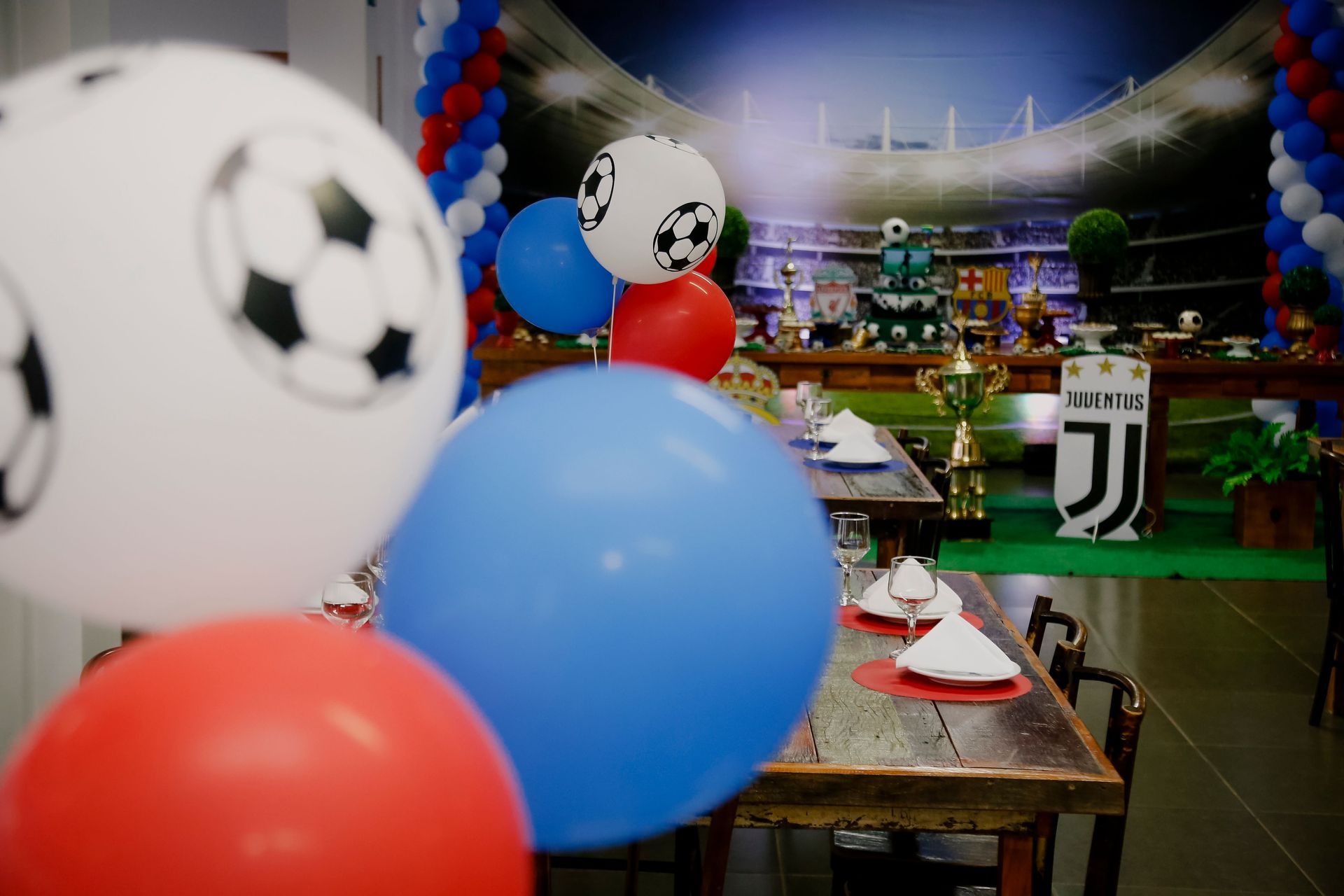 Table de fête sur le thème du football, avec des ballons rouges, bleus et blancs, dans une salle décorée.