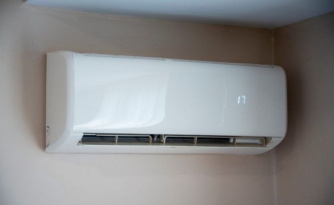Aire acondicionado blanco montado en la pared sobre una pared beige cerca del techo.