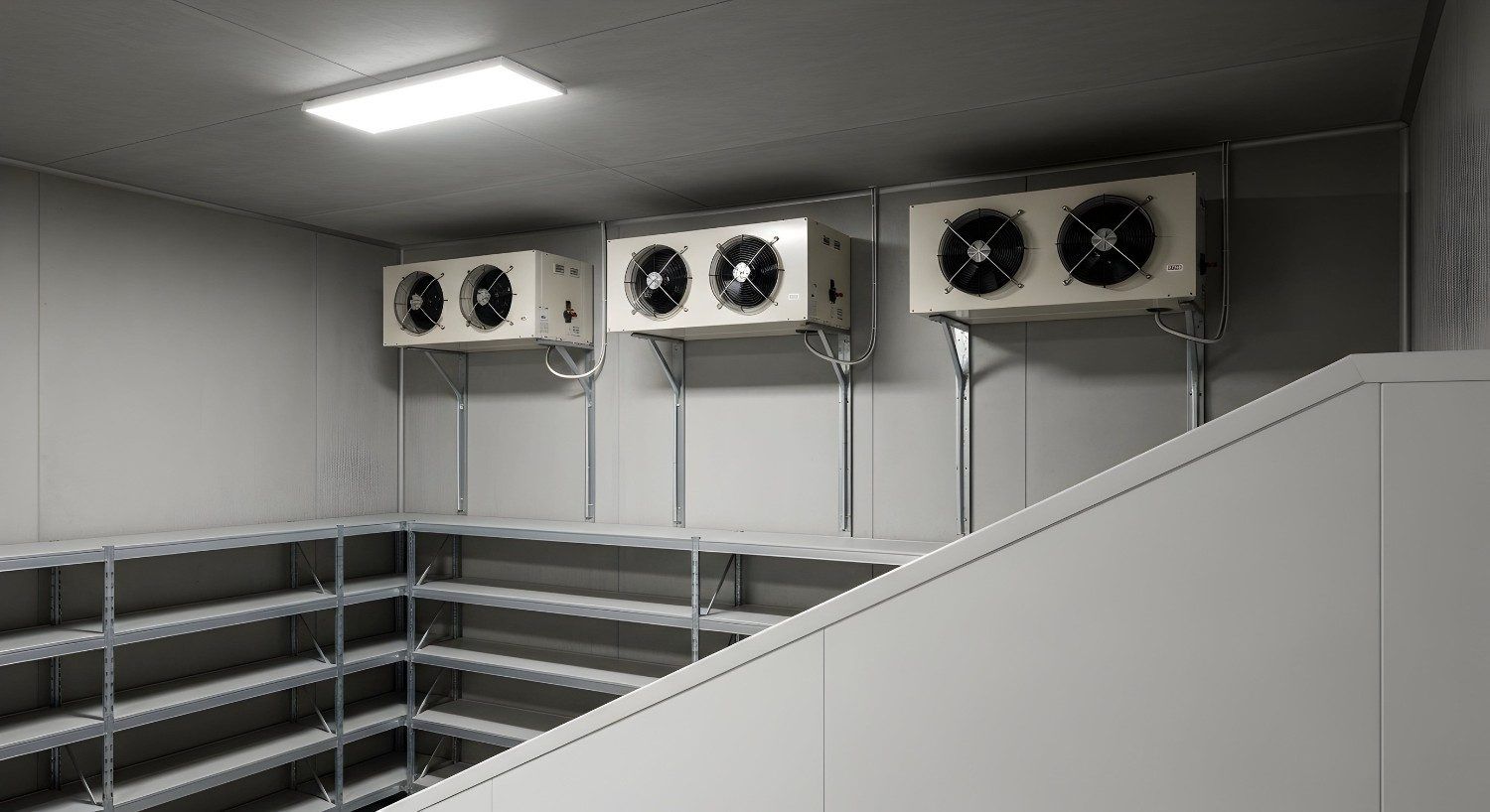 Interior con unidades de refrigeración industrial montadas sobre estanterías metálicas de almacenamiento y una barandilla de escalera blanca.