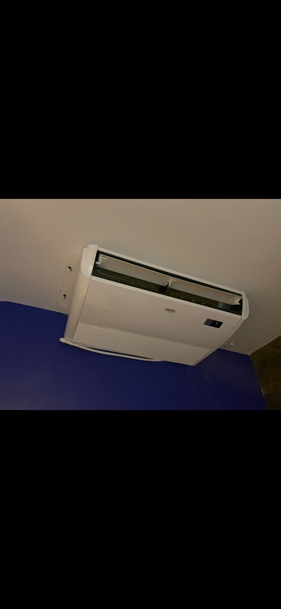 Aire acondicionado montado en la pared cerca del techo en una pared azul y blanca.