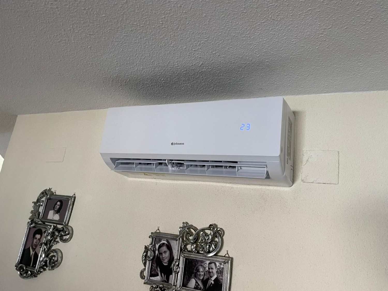 Aire acondicionado blanco montado en la pared sobre un cuadro decorativo en una pared de color claro.