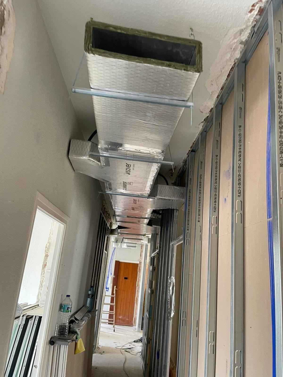 Pasillo estrecho en construcción con conductos de climatización plateados a la vista a lo largo del techo.