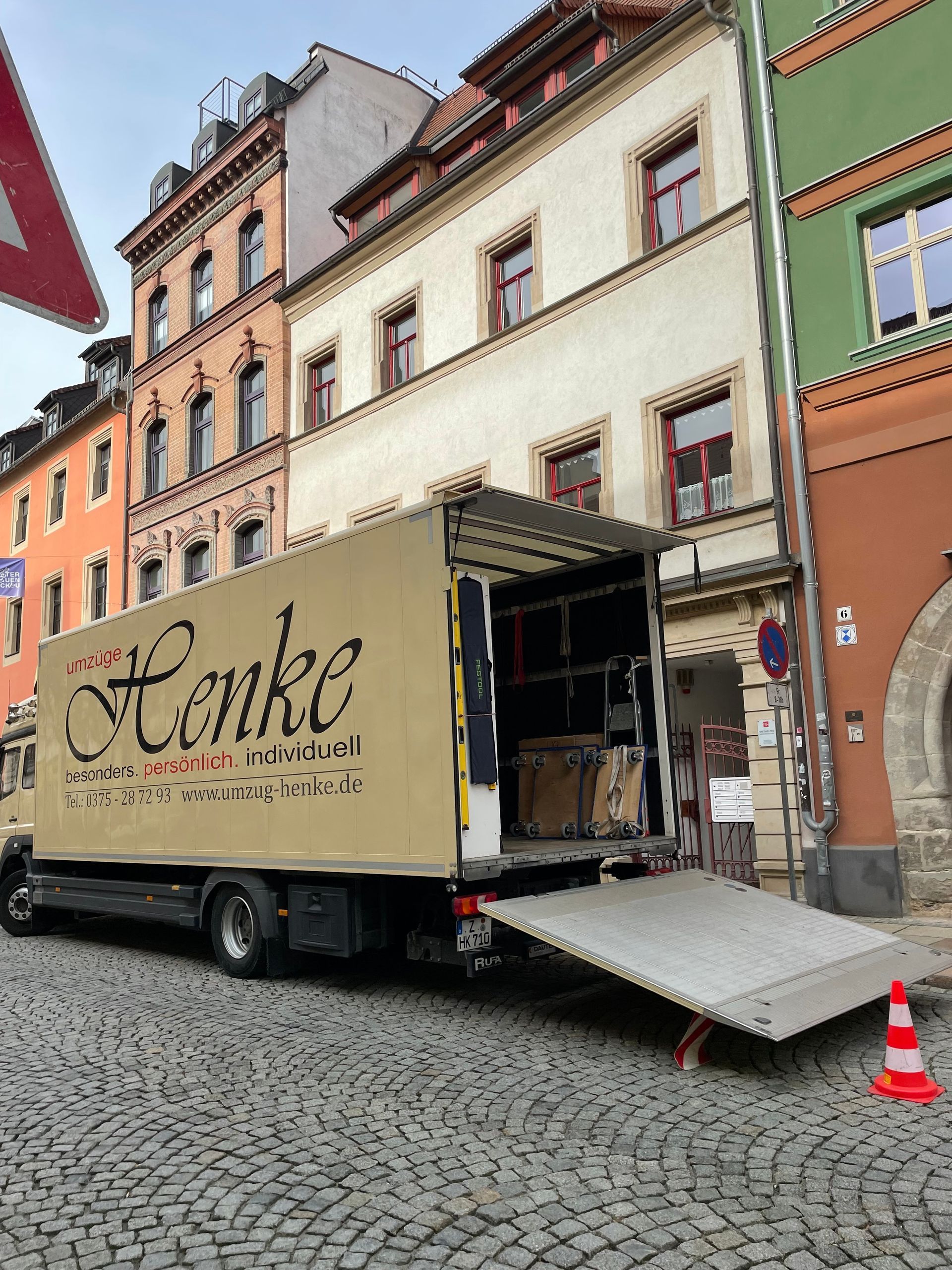 Umzugswagen in einer Altstadtstraße vor farbigen Wohnhäusern.