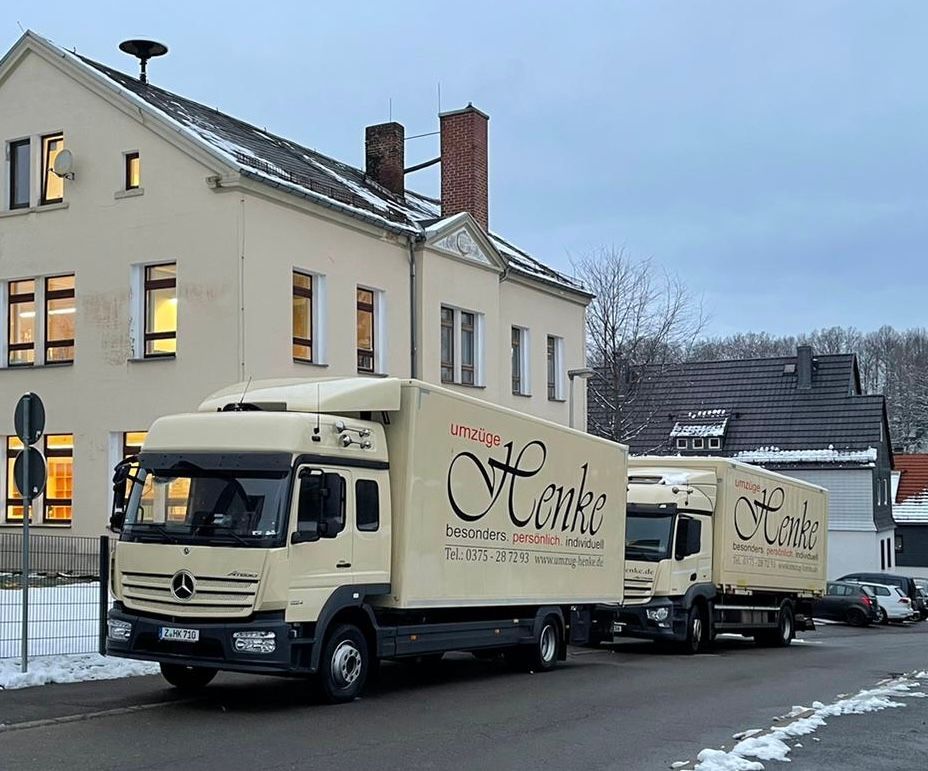 Zwei Umzugsfahrzeuge parken vor einem Wohngebäude im Winter.