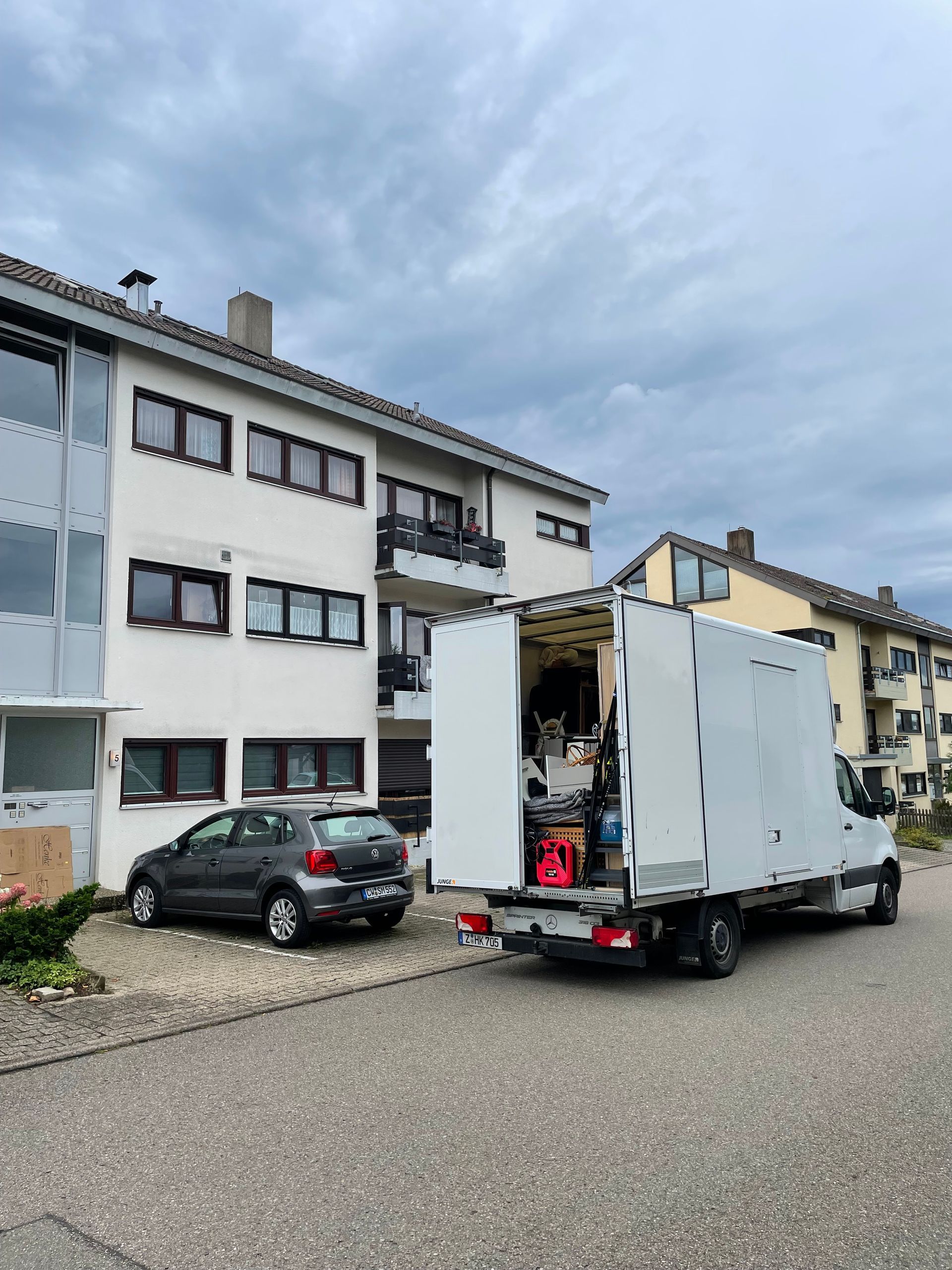 Kleiner Umzugswagen mit geöffneter Ladefläche vor einem Wohnhaus.