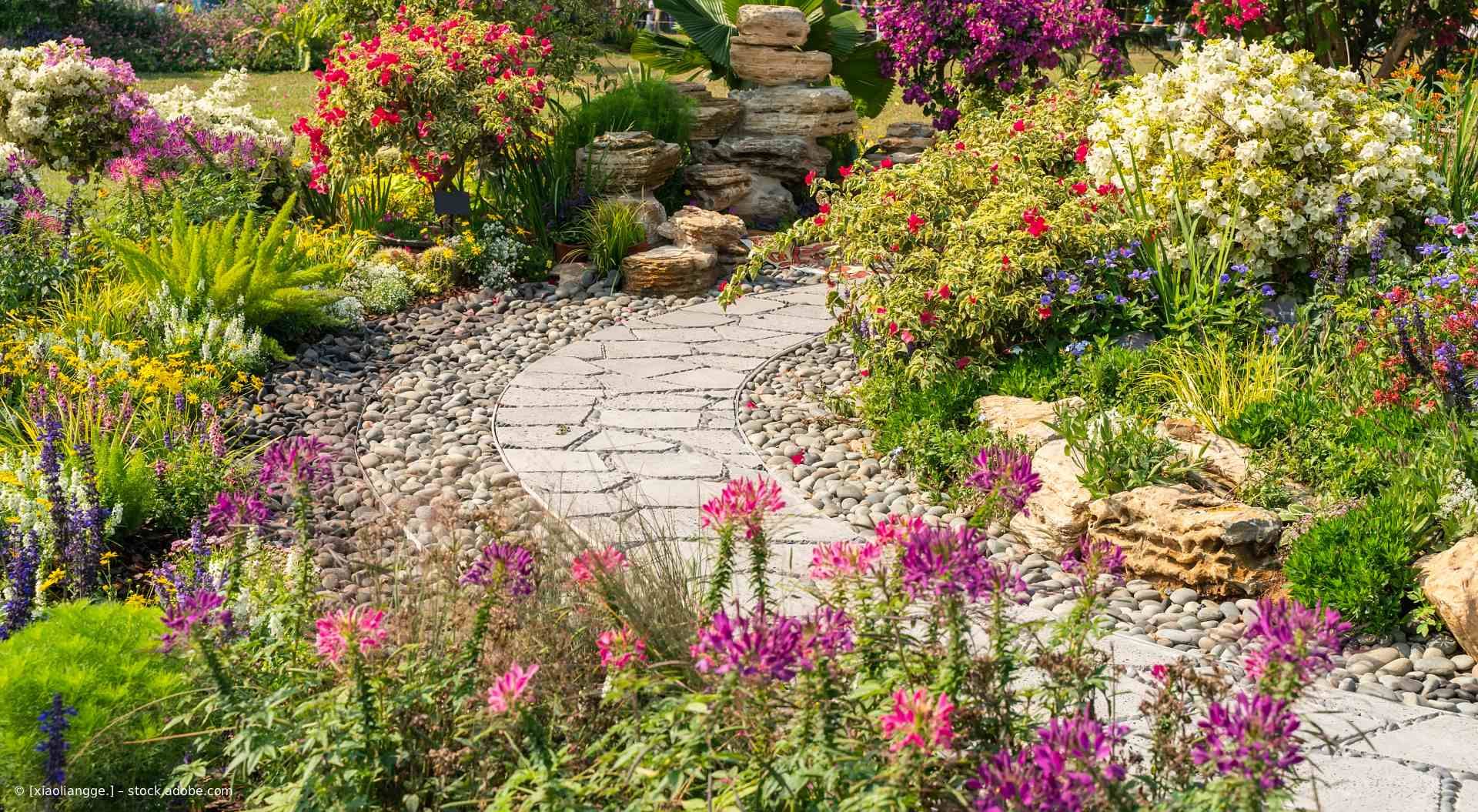Ein Steinpfad schlängelt sich durch einen lebendigen Garten mit farbenprächtigen Blumen und Felsformationen.