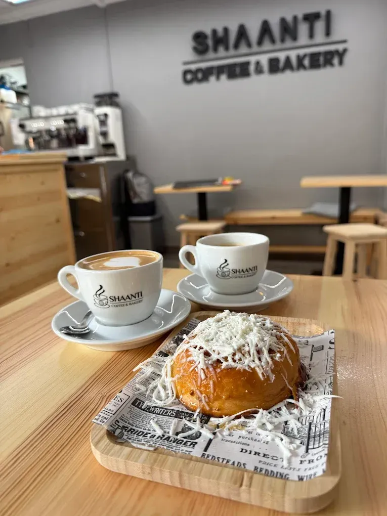 Dos tazas de café y un pastel en una mesa de madera en SHAANTI Coffee & Bakery.