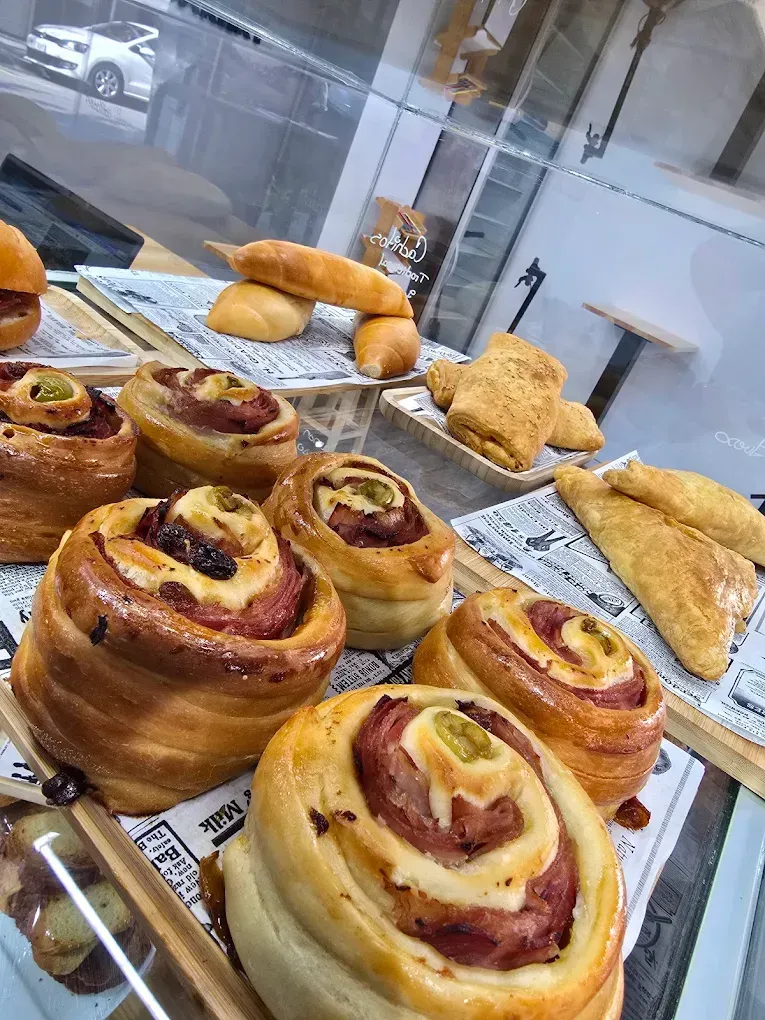 Variedad de pasteles y rollos de canela expuestos en una vitrina de panadería tras un cristal.