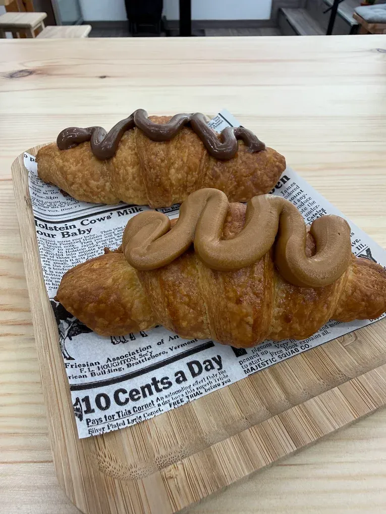Dos croissants de chocolate y dos de color beige cubiertos con glaseado en una bandeja forrada con papel de periódico.