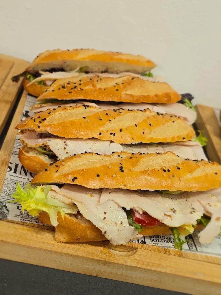 Tres sándwiches apilados en una bandeja de madera, con baguettes tostadas y lechuga a la vista.