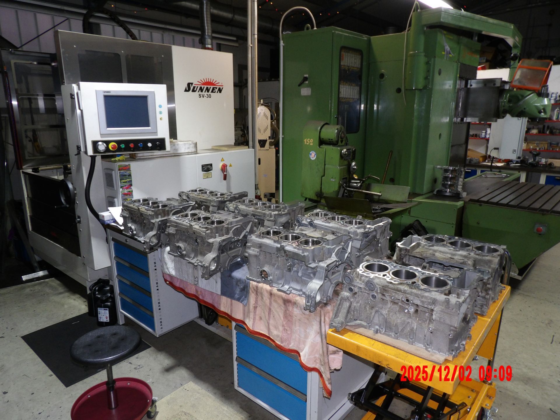 Metallene Motorblöcke auf einer Werkbank in einer Maschinenwerkstatt, neben einer CNC-Maschine.