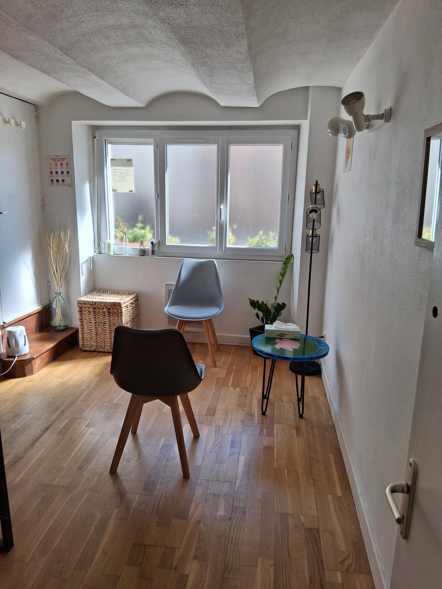 Une pièce avec deux chaises, une petite table, une fenêtre et un parquet.