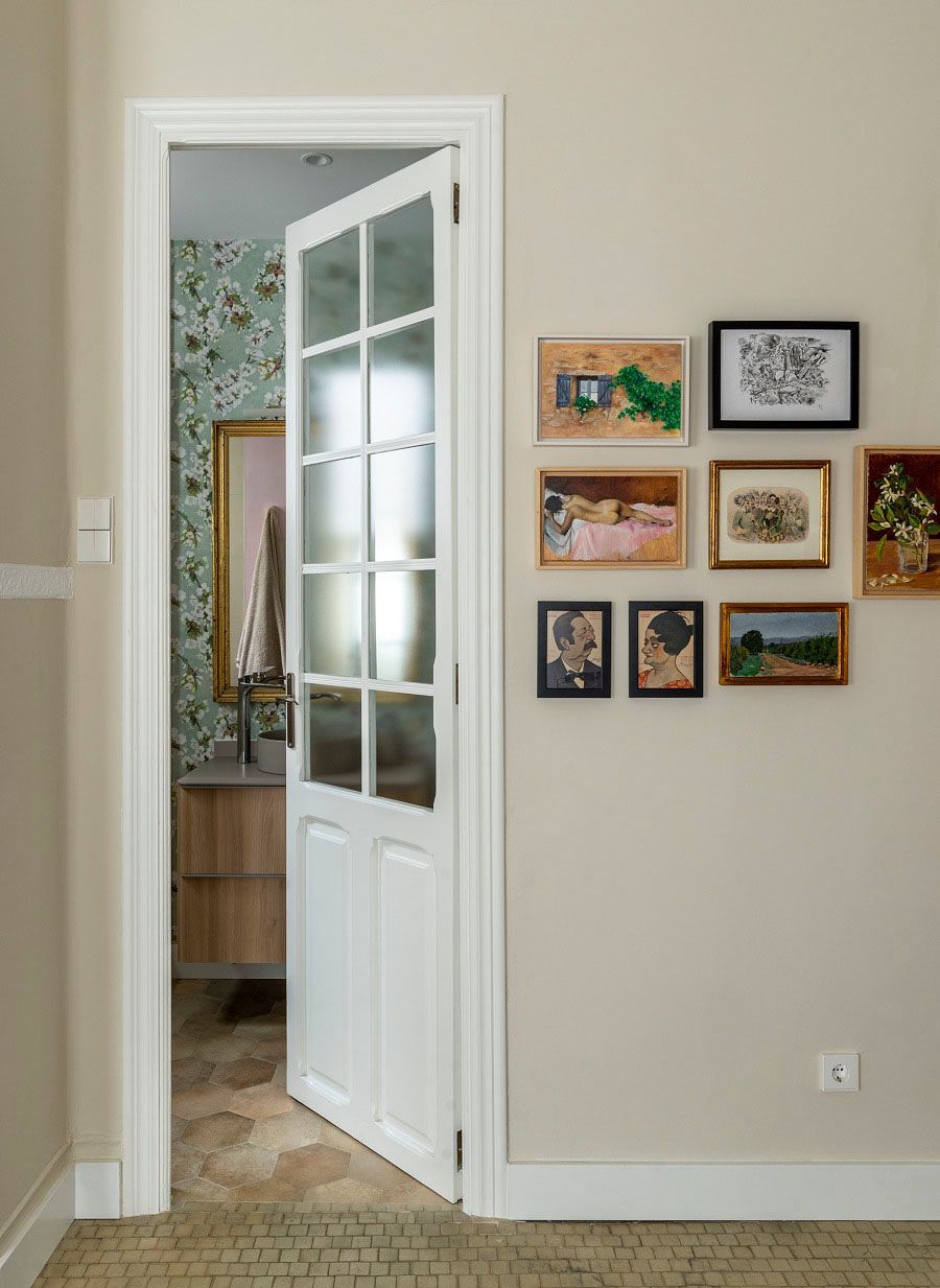 Una puerta blanca se abre a un baño con cuadros en la pared.