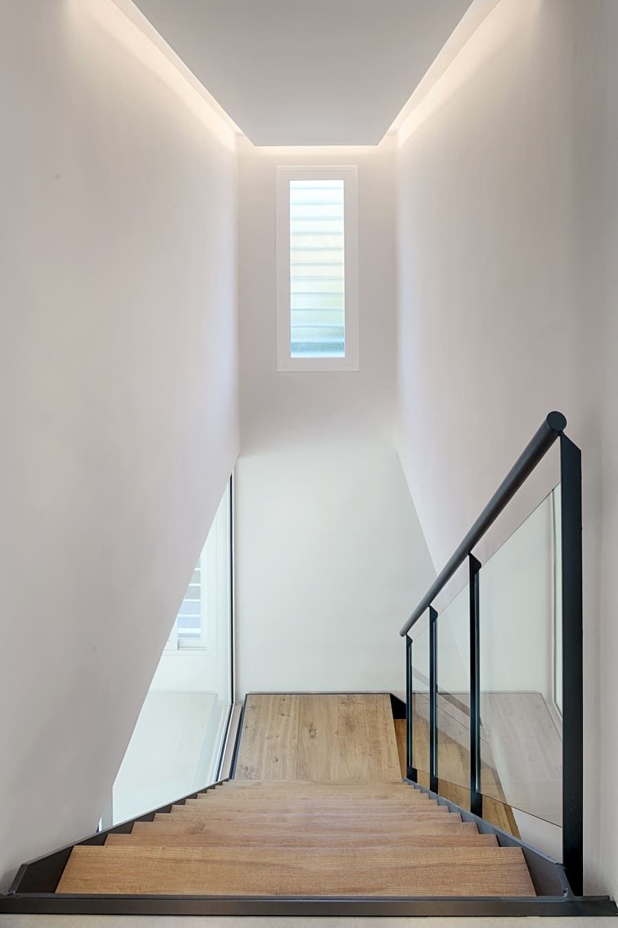 Una escalera de madera con barandilla de cristal y una ventana en el techo.