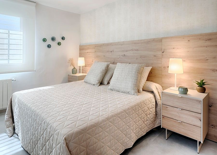 Un dormitorio con una cama, mesita de noche, lámparas y una ventana.