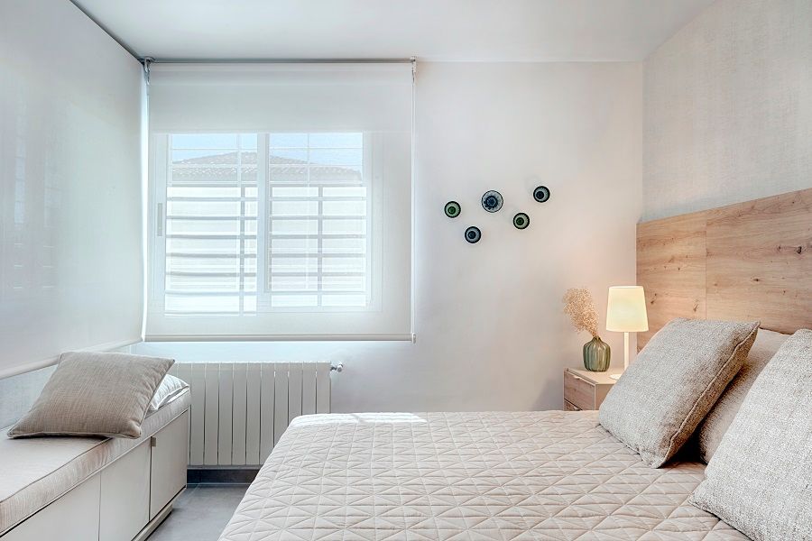 Un dormitorio con cama, mesita de noche, lámpara y ventana.