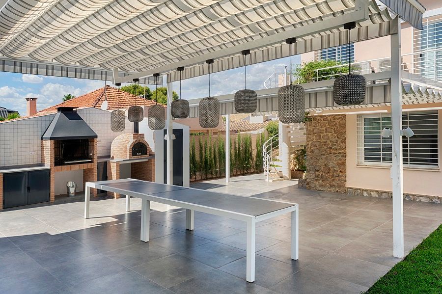 Un patio con mesa y parrilla bajo una pérgola.