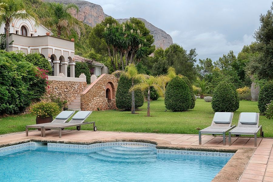 Una gran piscina rodeada de sillas y una casa al fondo.