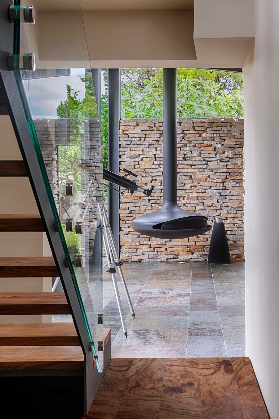 Una escalera con barandilla de cristal y una chimenea colgando del techo.