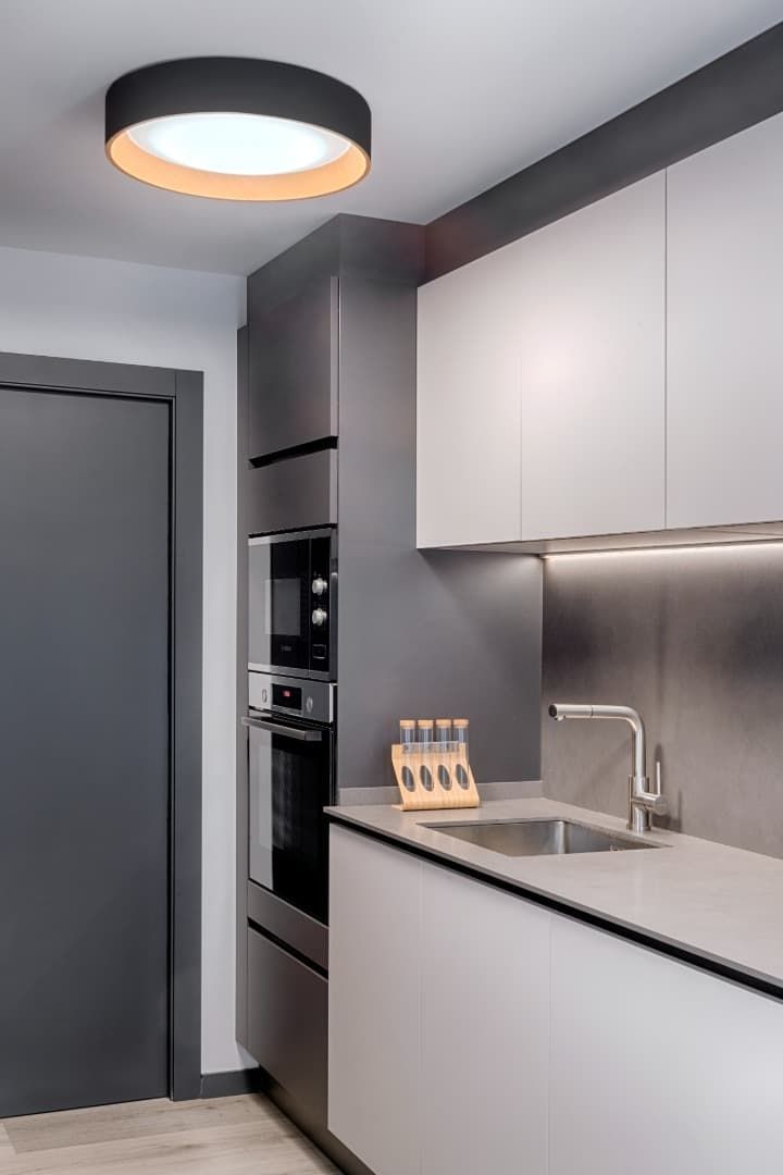 Cocina moderna gris con gabinetes blancos, horno empotrado, fregadero y luz de techo.
