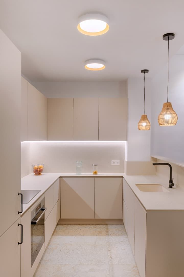 Cocina moderna blanca con lámparas colgantes, gabinetes beige y encimera en forma de L.