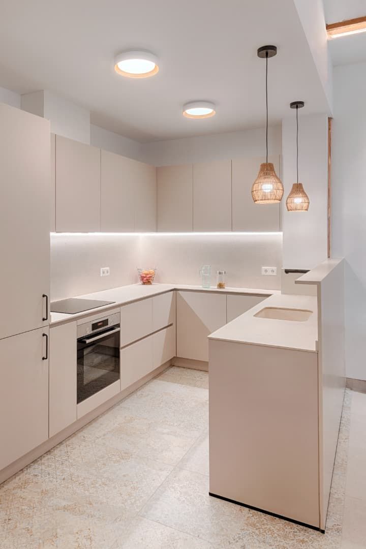 Cocina moderna y luminosa de color blanco con isla, horno empotrado y lámparas colgantes.