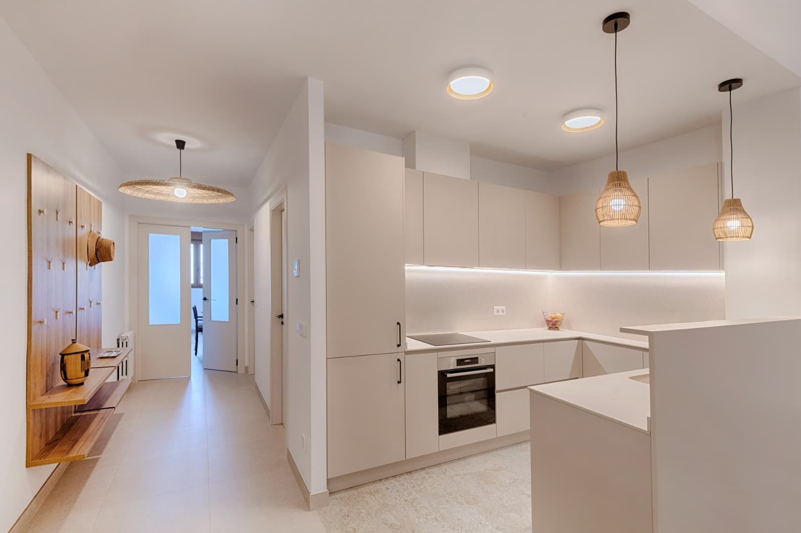 Cocina y pasillo modernos y luminosos en color blanco con lámparas colgantes y diseño diáfano.