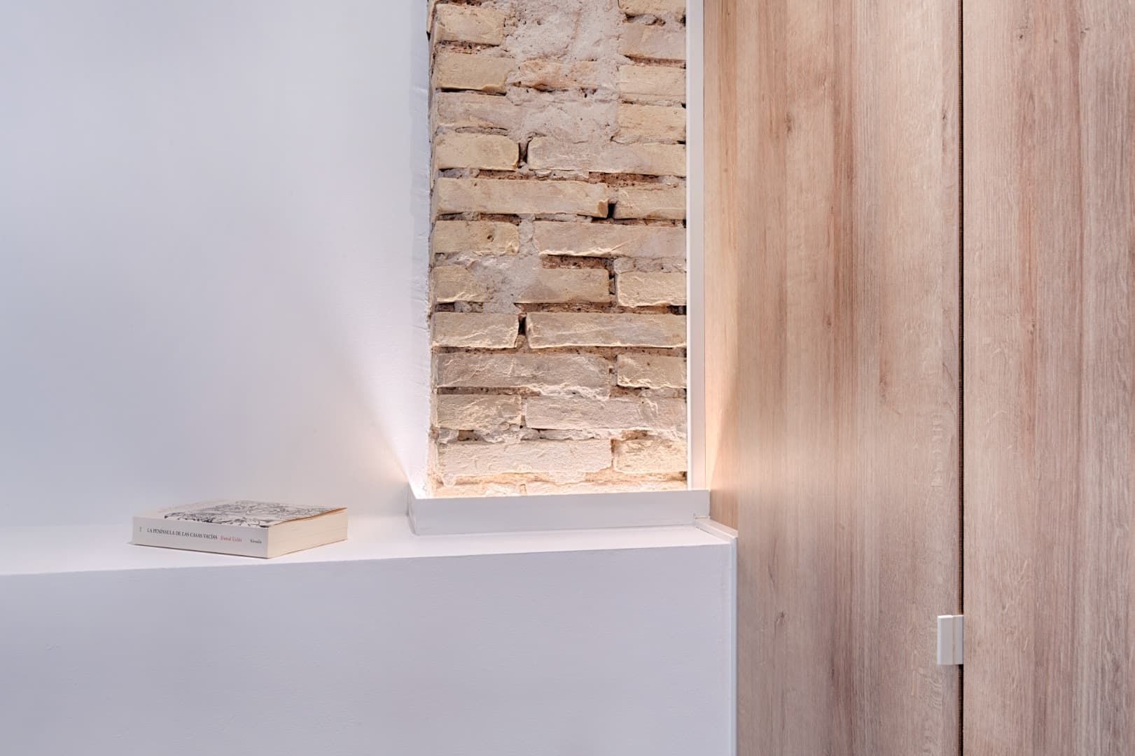 Decoración minimalista con estante blanco, ladrillo visto y paneles de madera clara.