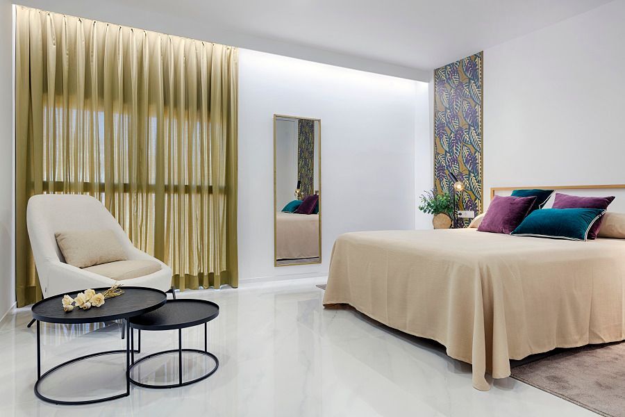 Un dormitorio con una cama grande, dos mesas de café, una silla y un espejo.