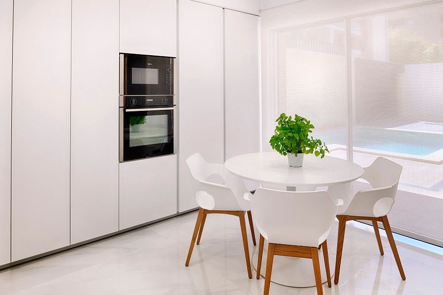 Una cocina con muebles blancos, una mesa redonda y sillas.