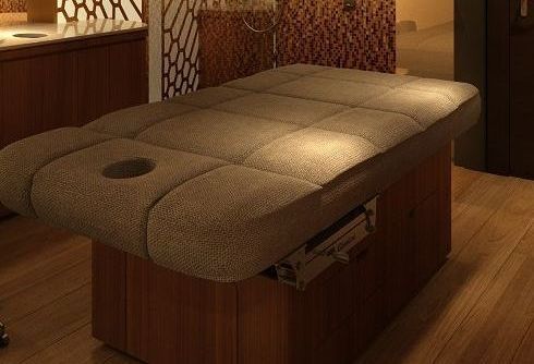 Una mesa de masajes está colocada sobre un suelo de madera en una habitación.
