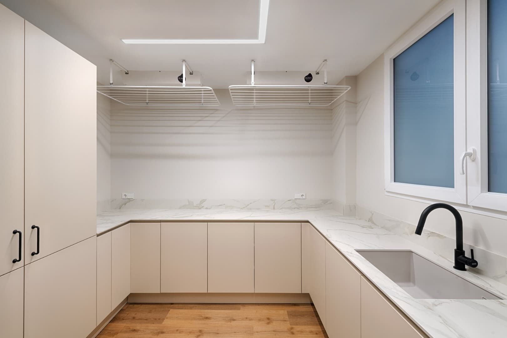 Cocina moderna blanca con encimeras de mármol, suelo de madera, fregadero, grifo negro y estanterías abiertas.