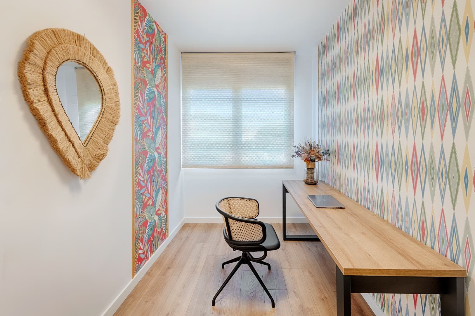 Pequeña oficina en casa con una silla, escritorio de madera, papel tapiz estampado y espejo de pared tejido.