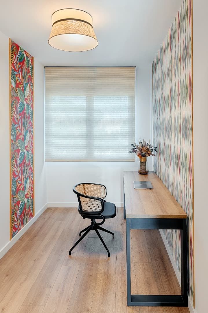 Un pequeño despacho en casa con escritorio, silla, persianas y papel pintado con estampados coloridos.