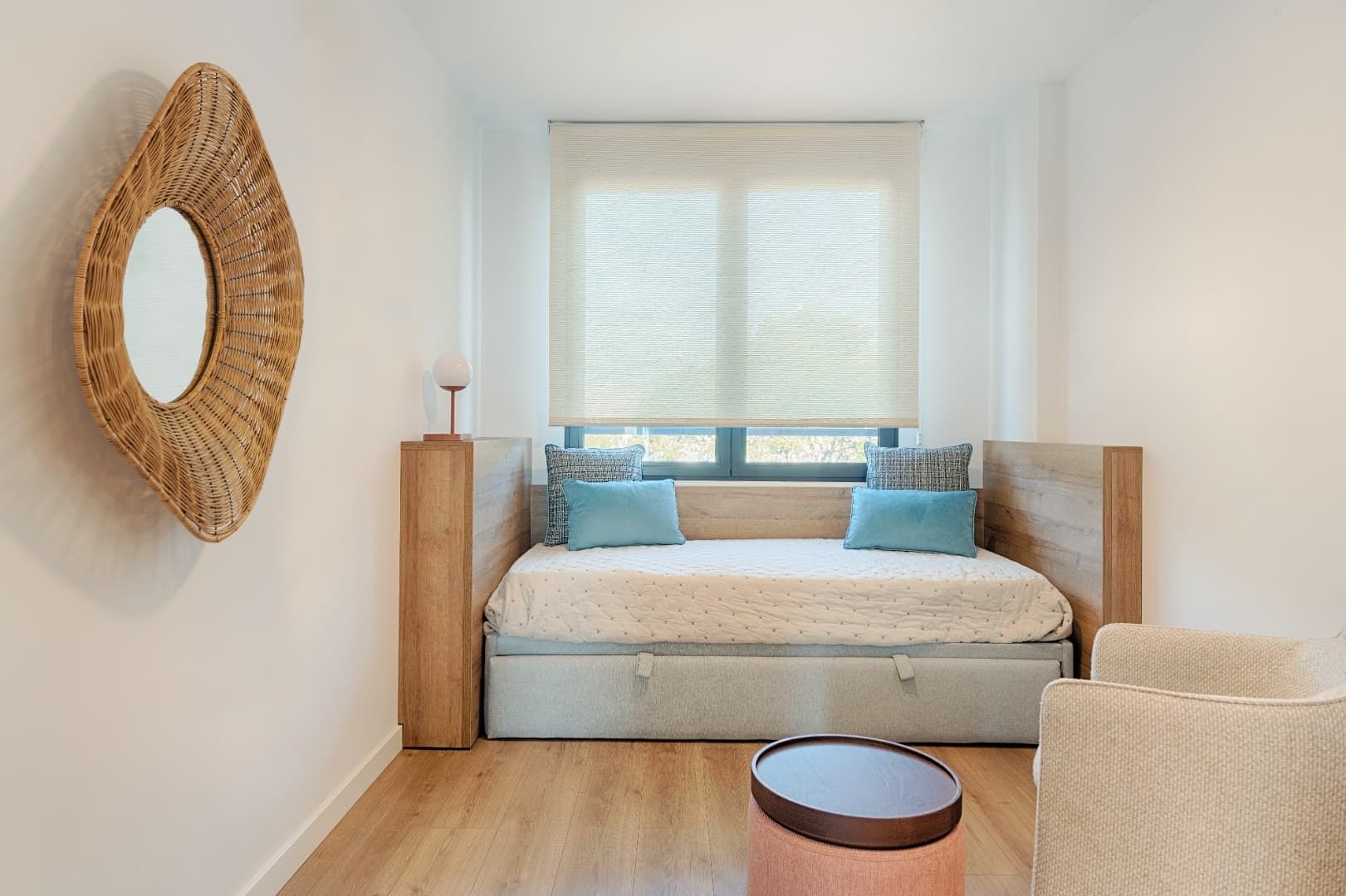 Dormitorio luminoso y minimalista con diván, espejo de pared tejido y detalles en madera clara.